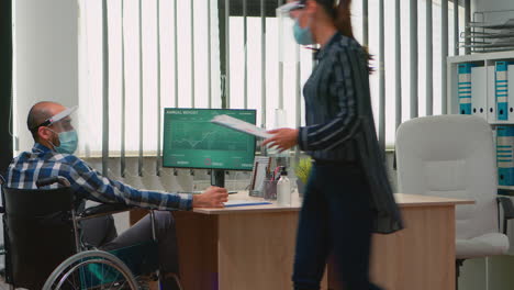 Businessman-with-mask-moving-with-wheelchair-in-workplace