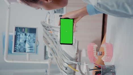 Vertikales-Video:-Zahnarzt-Blickt-Auf-Mobiltelefon-Mit-Grünem-Bildschirm