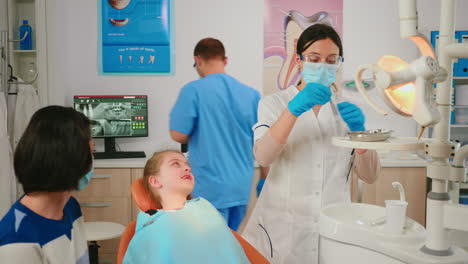 Stomatologe-Hält-Sterilisierte-Zahnarztinstrumente-In-Der-Hand-Und-Spricht-Mit-Einem-Kleinen-Patienten