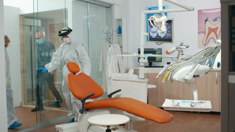 Nurse-with-protection-suit-inviting-patient-in-dental-room