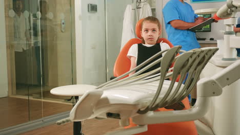 Little-girl-patient-waiting-pediatric-stomatologist-woman-sitting-in-dental-chair