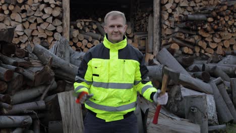 Lumberjack-in-reflective-jacket.-Man-woodcutter-holds-small-axe-and-saw-on-his-hands.-Firewood