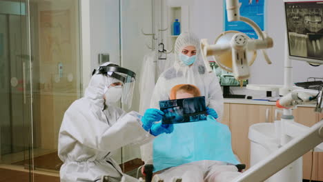 Doctor-in-protective-suit-discussing-about-x-ray-of-tooth-with-mother-of-child