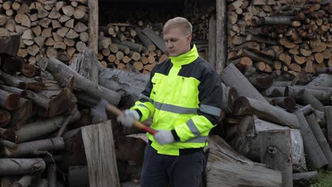 Lumberjack-in-reflective-jacket.-Man-woodcutter-hold-small-axe,-show-thumb-up.-Sawn-logs,-firewood