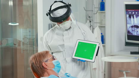 Dentist-in-coverall-pointing-at-green-screen-display-in-dental-unit