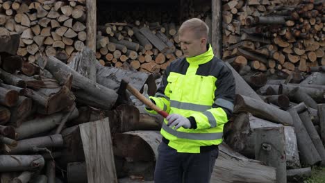 Lumberjack-in-reflective-jacket.-Man-woodcutter-hold-small-axe,-show-ok-sign.-Sawn-logs,-firewood