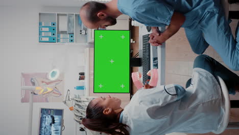 Vertical-video:-Dentist-and-assistant-looking-at-green-screen-on-computer