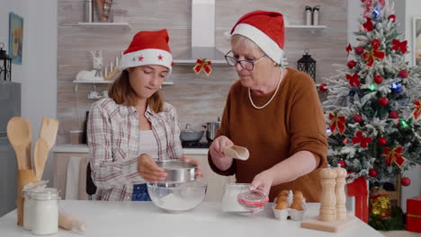 Granddaughter-putting-flour-ingredient-in-strainer-while-granddaughter-sift