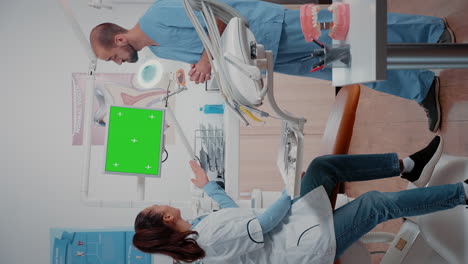 Vertical-video:-Dentist-and-assistant-working-with-green-screen-on-display