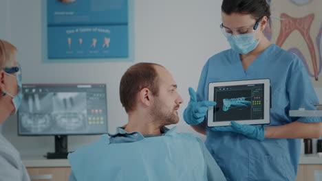 Dentistry-assistant-showing-x-ray-scan-results-on-tablet-to-patient
