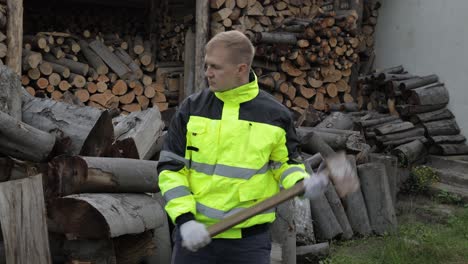 Lumberjack-in-reflective-jacket.-Man-woodcutter-hold-huge-axe-show-ok-sign.-Sawn-logs,-firewood