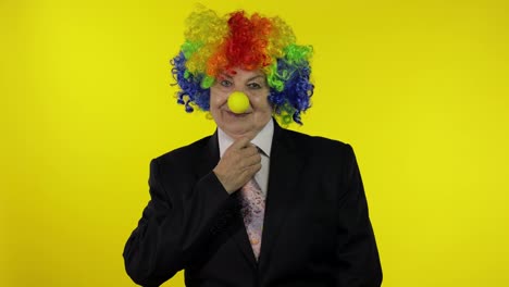 Senior-elderly-clown-businesswoman-boss-in-wig-adjusts-tie.-Yellow-background