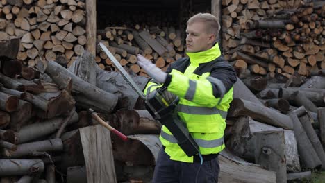 Lumberjack-in-reflective-jacket.-Man-woodcutter-with-electric-chainsaw.-Sawn-logs,-firewood,-sawmill