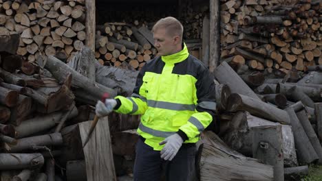 Lumberjack-in-reflective-jacket.-Man-woodcutter-hold-small-axe.-Sawn-logs,-firewood-background