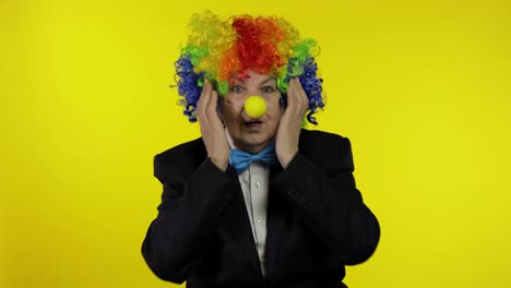 Senior-old-woman-clown-in-colorful-wig-looks-surprised-shocked.-Amazement