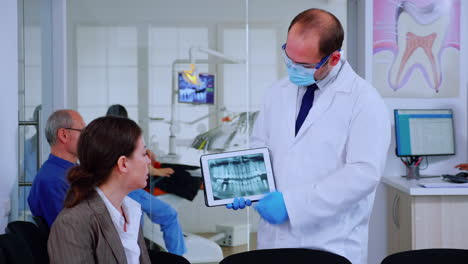 Stomatologist-pointing-on-digital-screen-explaining-x-ray-to-woman