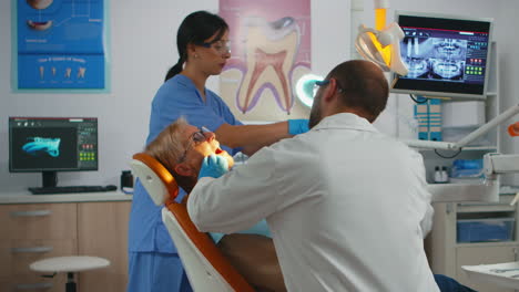 Dentista-Trabajando-En-Unidad-Dental-Con-Enfermera-Y-Paciente-Hombre-Acostado