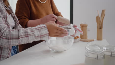 Closeup-of-grandmother-hands-putting-flour-in-strainer-while-granddaughter-sift-ingredient