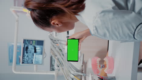 Vertical-video:-Specialist-analyzing-mobile-phone-with-green-screen