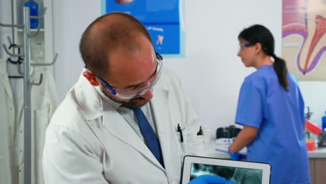 Médico-Sosteniendo-Una-Tableta-Con-Radiografía-De-Mandíbula-Mostrándola-Al-Paciente