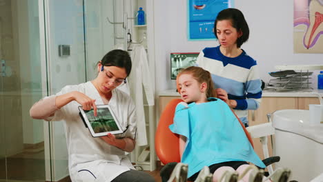 Orthodontist-holding-tablet-and-showing-jaw-x-ray-to-little-patient