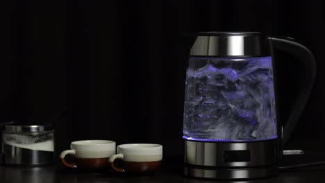 Boiling-water-in-glass-transparent-electric-kettle-with-blue-light-illumination.-Black-background