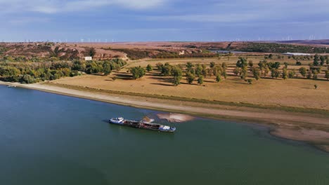 Aerial-wide-shot-of-a-dredger-unloading-dredged-sand-on-a-big-river,-sunny-day