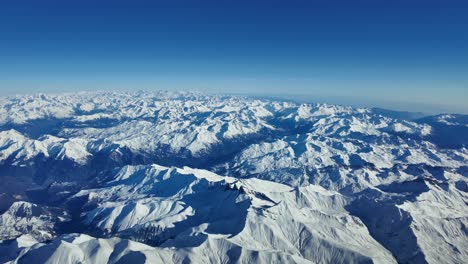 Breathtaking-aerial-view-of-the-snowy-Alps-mountains-shot-from-an-airplane-cabin,-as-seen-by-the-pilots-while-flying-across-a-bright-and-sunny-winter-day-at-8000m-high