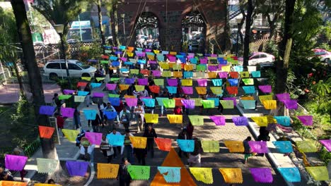 Aerial-view-dolly-out-of-a-cobblestone-street-decorated-with-colorful-ribbons-hanging,-festival-of-a-group-of-people-in-Iztapalapa-CDMX,-Mexico