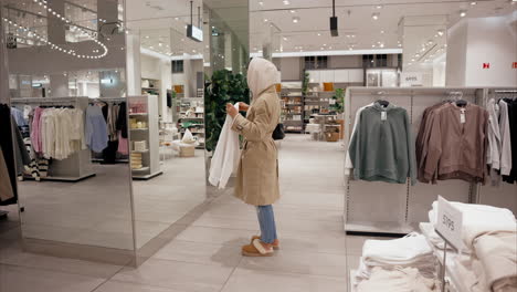 Hipster-influencer-girl-is-shopping-for-winter-clothes-and-trying-on-a-sweater-at-the-store