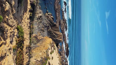 Praia-de-Almograve-beach-with-ocean-waves,-cliffs-and-stones,-wet-golden-sand-and-green-vegetation-at-wild-Rota-Vicentina-coast,-Odemira,-Portugal