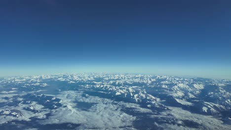 Aerial-view-of-the-snowy-Alps-mountains-shot-from-a-jet-cockpit-while-flying-across-a-bright-and-blue-sky