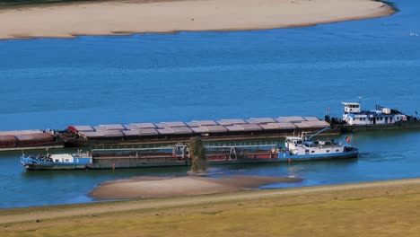 Aerial-close-up-shot-of-a-dredger-unloading-dredged-sand-on-a-big-river,-other-ships-passing-by,-sunny-day