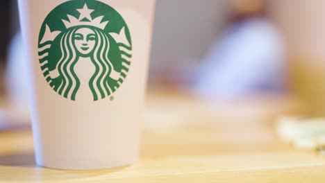 Un-Café-Starbucks-En-El-Primer-Plano-Del-Cuadro-Mientras-Un-Hombre-Negro-Afroamericano-Corpulento-En-El-Fondo-Borroso-Está-Conversando