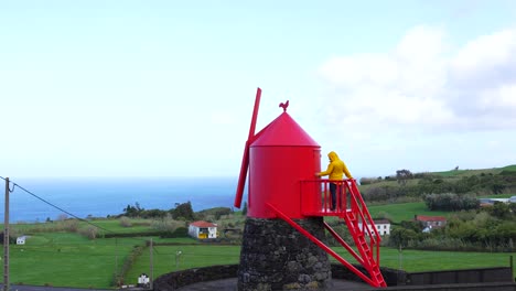 Man-on-traditional-and-red-windmill-at-coast-of-Faial-island,-Azores,-Portugal