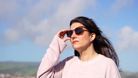 Woman-wearing-sunglasses-being-dazzled-by-the-sun-in-a-windy-day,-handheld-shot