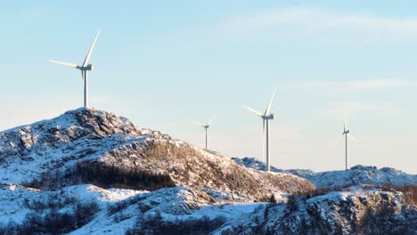 Wind-Turbines-on-Top-of-Snow-Capped-Mountain-Hills-on-Sunny-Winter-Day,-Establishing-Drone-Shot
