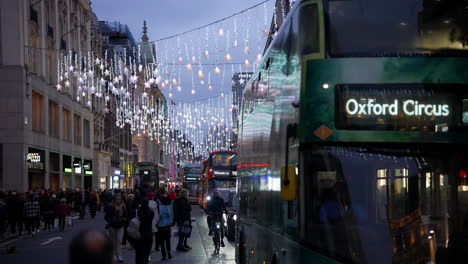 Ein-Grüner-Oxford-Zirkusbus-Der-Linie-55-Fährt-Los,-Während-Weihnachtseinkäufer-In-Der-Abenddämmerung-Die-Bürgersteige-Unter-Den-Festlichen-Lichtern-Der-Oxford-Street-Füllen