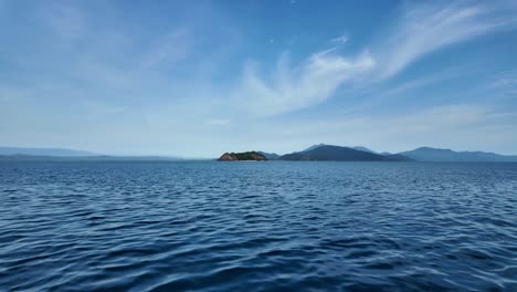 Fast-moving-boat-view-of-a-deserted-ocean-Island-with-a-mountain-and-blue-sky-backdrop