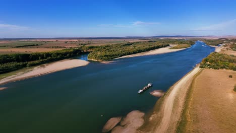 Aerial-wide-shot-of-a-dredger-unloading-dredged-sand-on-a-big-river,-sunny-day
