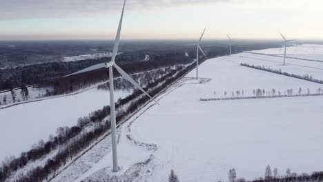 Aerial-view-of-rotating-wind-turbine-blades-in-winter-landscape-near-forest