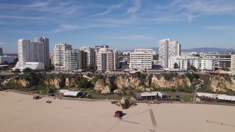 Popular-tourist-sandy-beach-Praia-da-Rocha-and-cliffs-in-Portimao,-residential-buildings,-fly-backwards