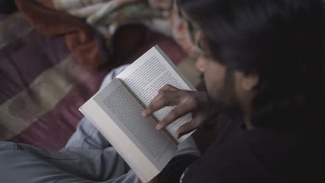 Un-Libro-De-Lectura-Indio-Del-Sur-De-Asia-En-Una-Habitación-Fría-Y-Oscura-Sentado-En-Una-Cama