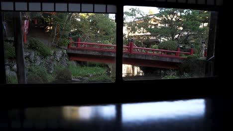Blick-Aus-Den-Ryokan-Shoji-Fenstern-Auf-Die-Rote-Brücke-über-Den-Koi-Teich-Im-Japanischen-Zen-Garten