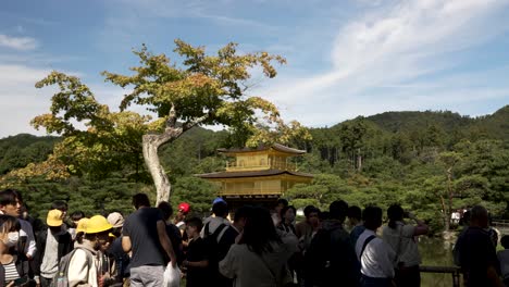 Busy-Crowds-Seen-Walking-Past-With-Kinkakuji-In-Background-On-Sunny-Day