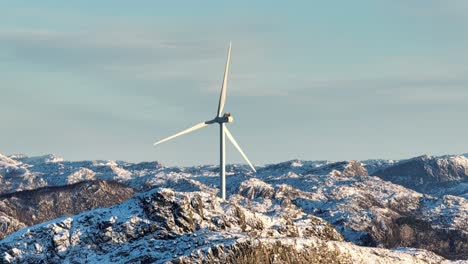 Drone-Shot-of-Wind-Turbine-Spinning-Above-Snow-Capped-Hills-on-Sunny-Winter-Day