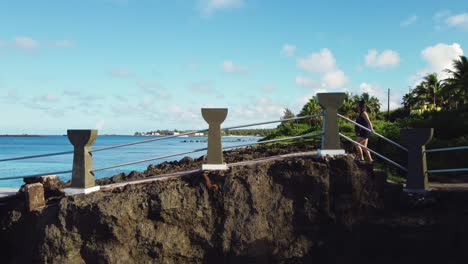 Drone-shot-of-a-girl-walking-towards-the-cliff-of-Taga-beach,-Tinian-Island