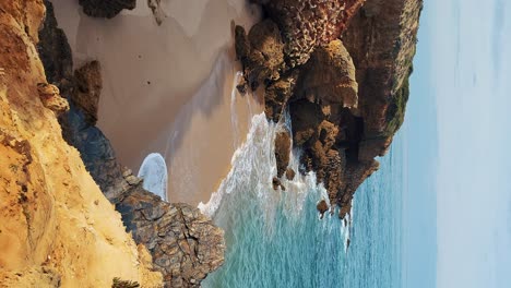 Praia-de-Almograve-beach-with-ocean-waves,-cliffs-and-stones,-wet-golden-sand-and-green-vegetation-at-wild-Rota-Vicentina-coast,-Odemira,-Portugal