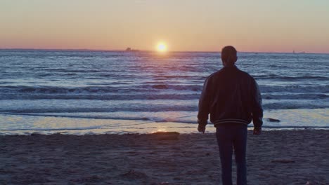 caucasian-male-man-model-walks-on-the-beach-near-the-sea-ocean-on-the-sand-shore-with-sunset-and-cinematic-actor's-play