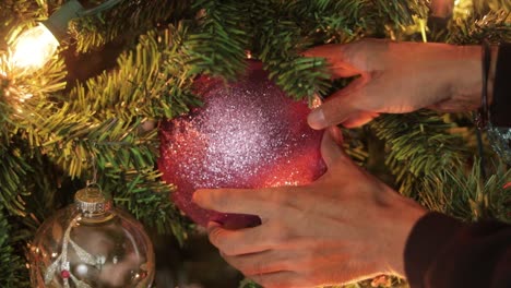Placing-large-pink-glitter-christmas-ball-on-decorated-christmas-tree